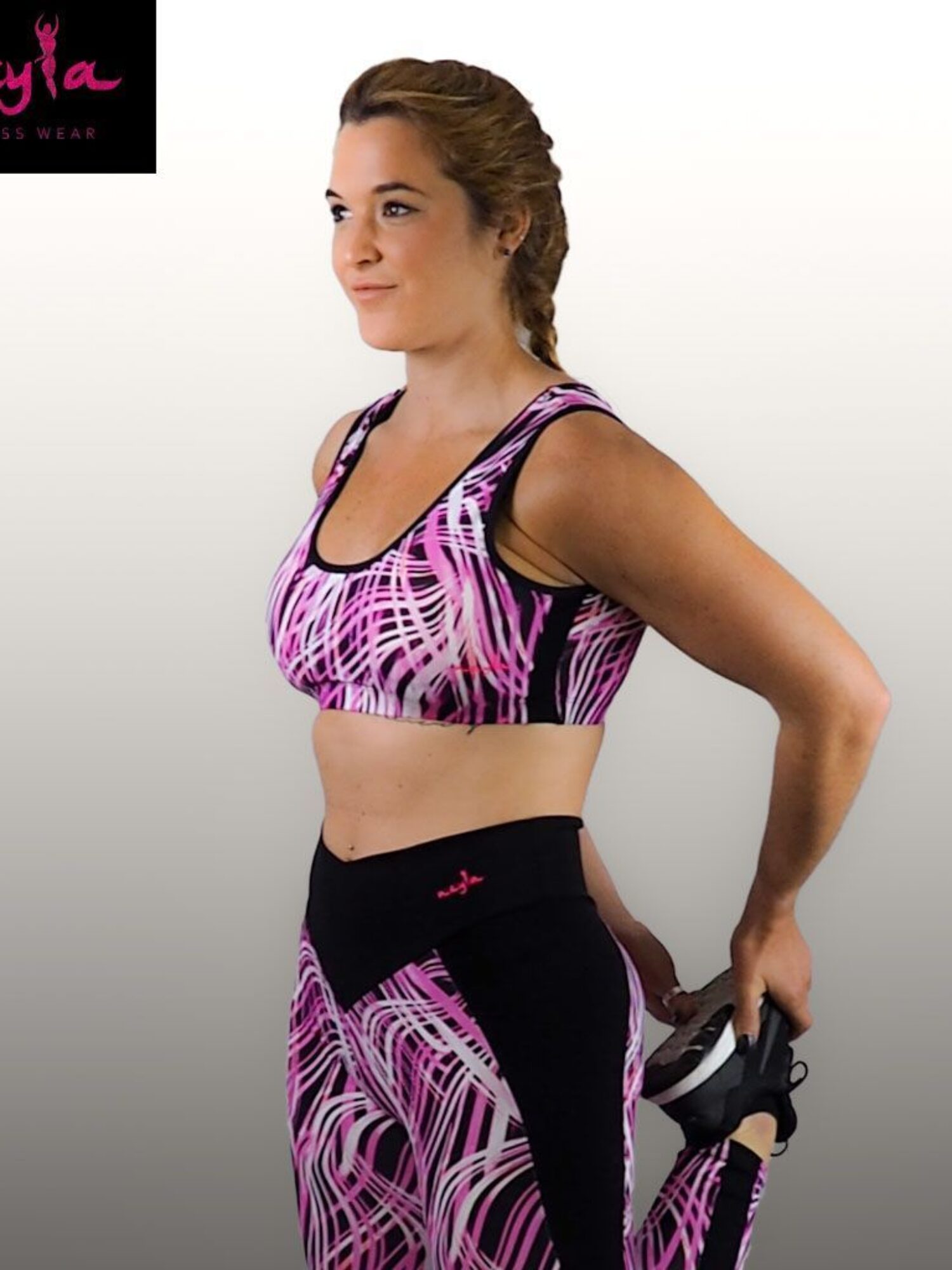 Mujer vistiendo conjunto fitness Rea con top de tirantes anchos estampado en rosa, blanco y negro y leggings de cintura alta con detalles negros.