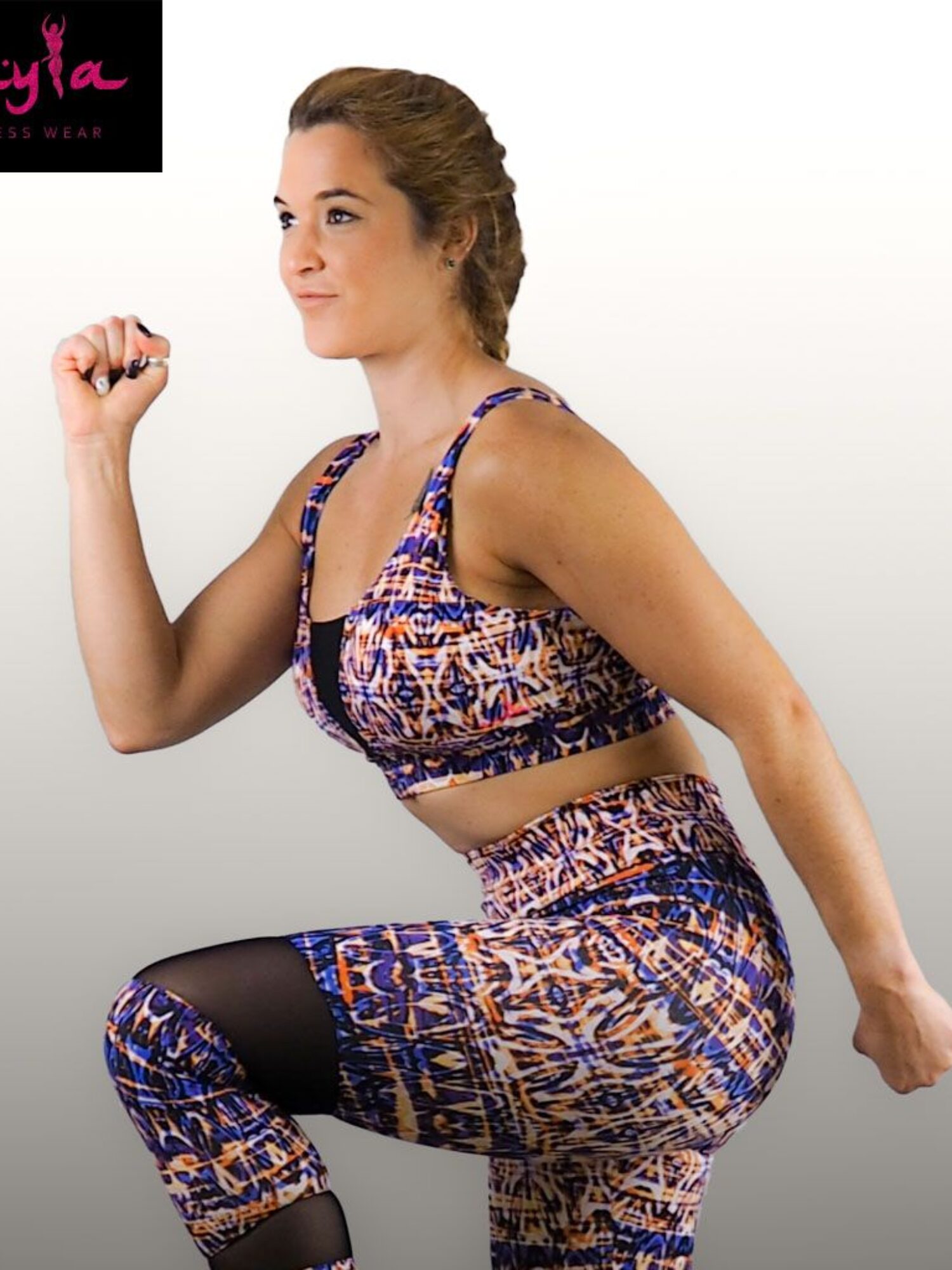 Mujer vistiendo conjunto fitness Metis con top de tirantes estampado azul y naranja y leggings de cintura alta con franjas de tul negro.