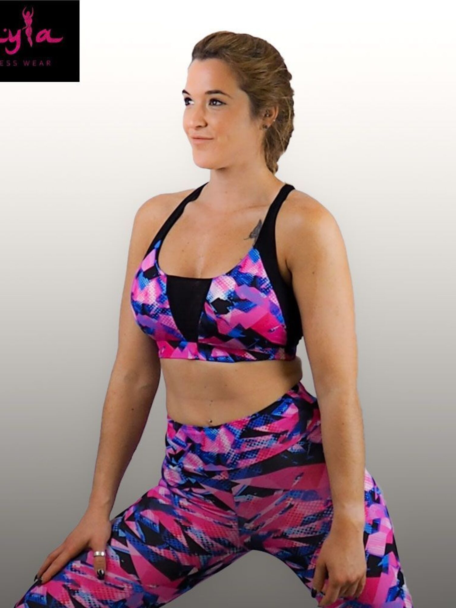 Mujer vistiendo conjunto fitness Nix con top de tirantes estampado rosa, azul y negro y leggings de cintura alta con franjas de tul negro.